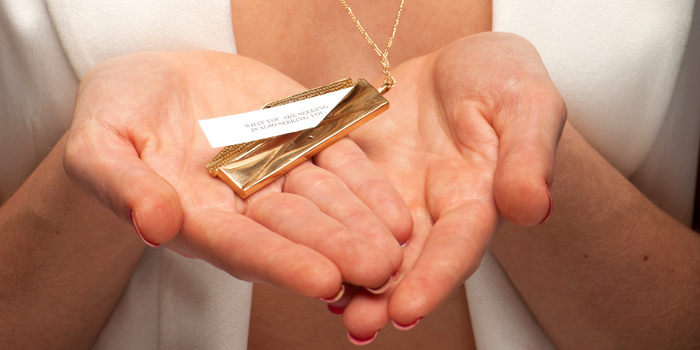 Two hands holding a gold, open envelope fortune locket with a message sticking out.